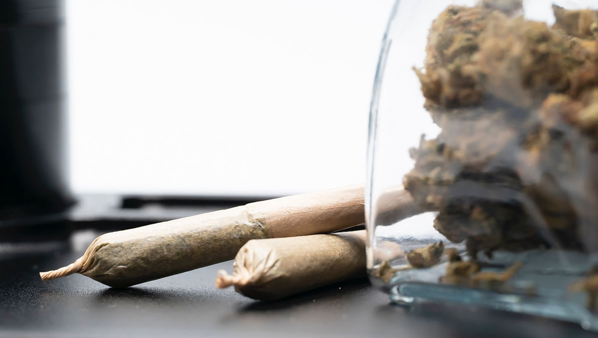 Thailand Lifts the Ban on Cannabis Opening the Floodgates of Legal Trade: A glass jar with marijuana buds and two pre-rolls lying next to it