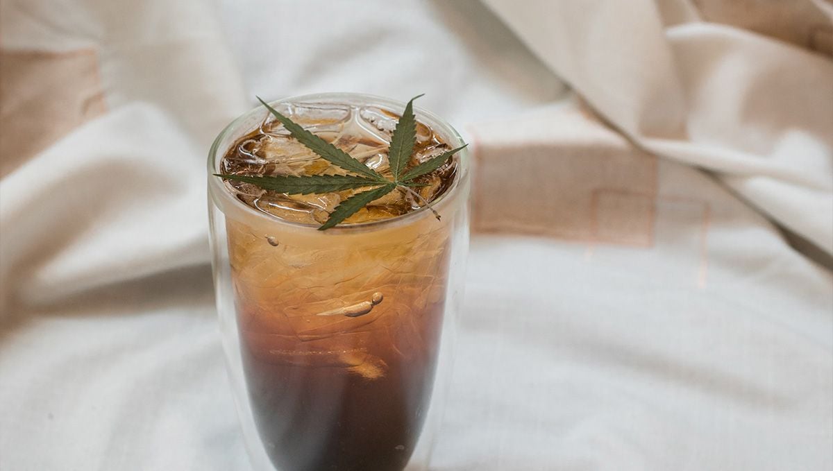THC Syrup Explained: What Is THC Lean & How to Make It: A brownish soft drink with ice in a tall transparent glass with a fresh marijuana leaf on top